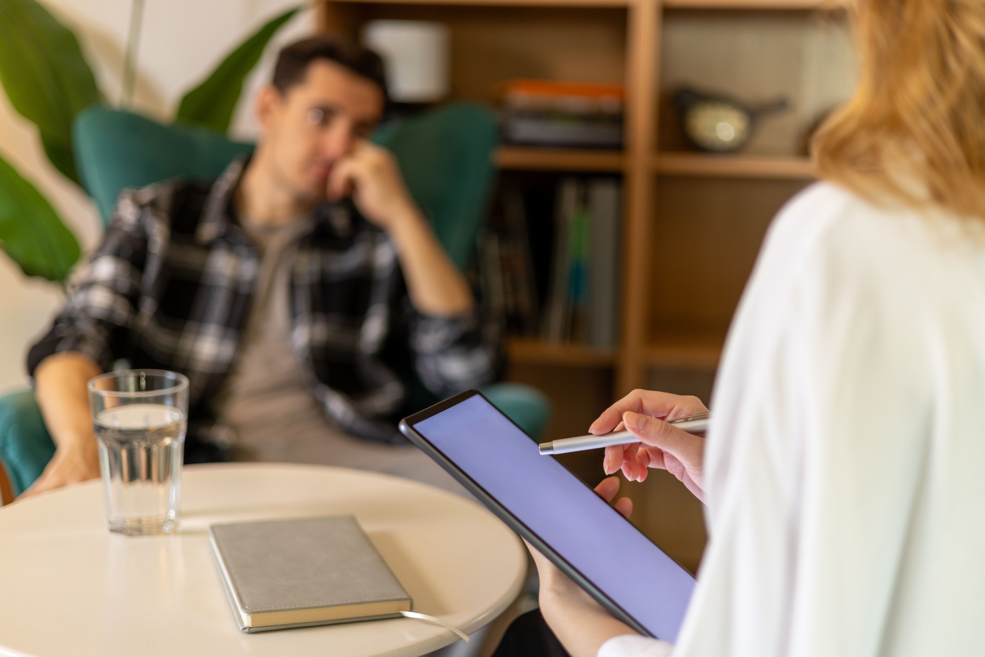 Psychologist using digital tablet and stylus pen, taking notes during a therapy session with a male patient